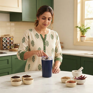 A South Asian woman using a compact GharMix mini grinder in a bright, modern kitchen with forest green and cream decor.